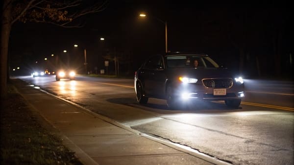 A car on a dark, empty rural road with its high beam headlights on, illuminating far into the distance