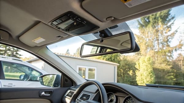 A driver and passenger both looking in their respective sun visor mirrors