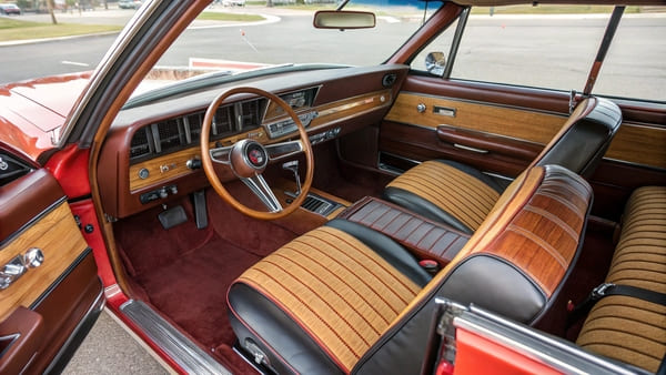 Interior of a 1970s car showing woodgrain trim and bold colored seats