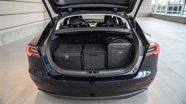 A Tesla Model 3 with its trunk open, parked in a suburban driveway